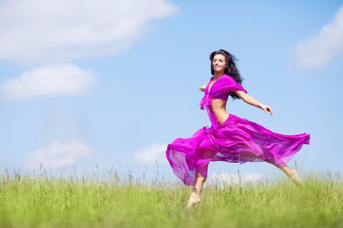 A woman in purple dress running through the grass.