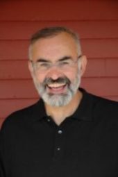 A man with grey hair and beard smiling for the camera.